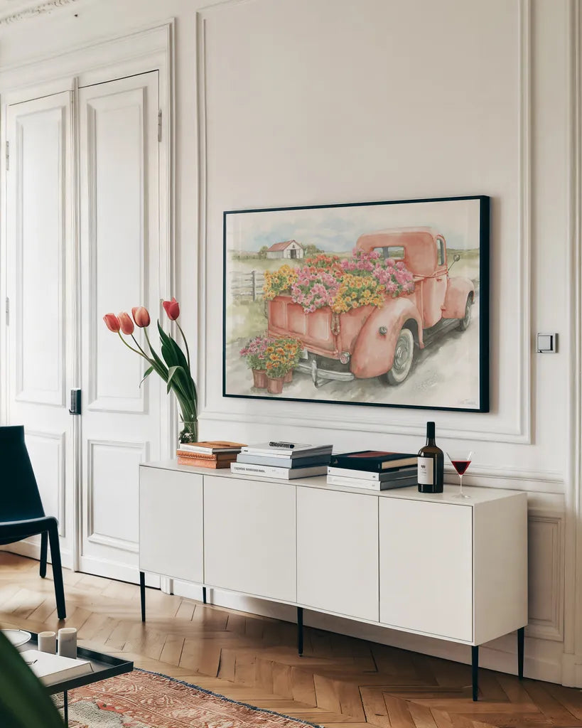 Red Truck with Flowers by Leslie Trimbach. shown as a framed stretched canvas in a living room above a console. Available as a archival giclee rolled canvas, fine art paper, or poster print. SKU 96646i.