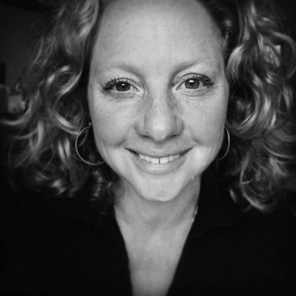 Black-and-white portrait of artist Belinda Aldrich, smiling at the camera with curly hair and hoop earrings. Contemporary designer and illustrator known for creative artwork