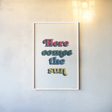 Rainbow Here Comes the Sun Bold by Becky Thorns. shown as a paper print in a white frame. Available as a archival giclee rolled canvas, fine art paper, or poster print. SKU 65214h.