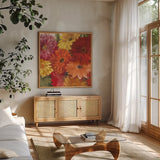 Bountiful Gerberas Square I by Carol Rowan. Shown in a natural wood frame in a cozy modern living room. Available as an archival giclee rolled canvas, fine art paper, or poster print. SKU 26991a.