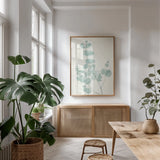 Eucalyptus Branch I by Chris Paschke. shown as a print in a natural wood frame in a dining room. Available as a archival giclee rolled canvas, fine art paper, or poster print. SKU 55063h.