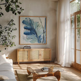 Luxe Banana Leaf I by Chris Paschke. Shown in a natural wood frame in a cozy modern living room. Available as an archival giclee rolled canvas, fine art paper, or poster print. SKU 84576a.
