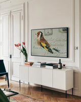 Goldfinch by Deborah Revell. shown as a framed stretched canvas in a living room above a console. Available as a archival giclee rolled canvas, fine art paper, or poster print. SKU 104183i.