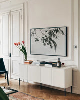 Simple Eucalyptus I by Deborah Revell. shown as a framed stretched canvas in a living room above a console. Available as a archival giclee rolled canvas, fine art paper, or poster print. SKU 102714i.