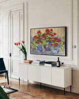 Red Geraniums with The Blues by Kathleen Parr McKenna. shown as a framed stretched canvas in a living room above a console. Available as a archival giclee rolled canvas, fine art paper, or poster print. SKU 88422i.