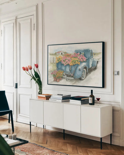 Truck with Flowers on Blue by Leslie Trimbach. shown as a framed stretched canvas in a living room above a console. Available as a archival giclee rolled canvas, fine art paper, or poster print. SKU 86547i.