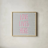 Love Lives Here Slate and Pink by Michael Mullan. Shown in a natural wood glass frame for a timeless modern aesthetic. Available as an archival giclee rolled canvas, fine art paper, or poster print. SKU 67444a.