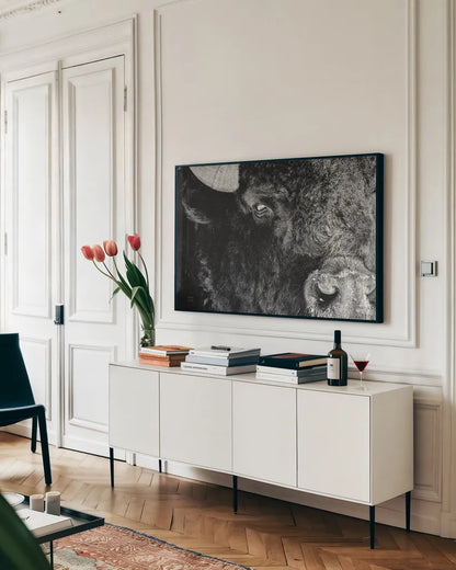 Bison Stare BW by Nathan Larson. shown as a framed stretched canvas in a living room above a console. Available as a archival giclee rolled canvas, fine art paper, or poster print. SKU 87948i.