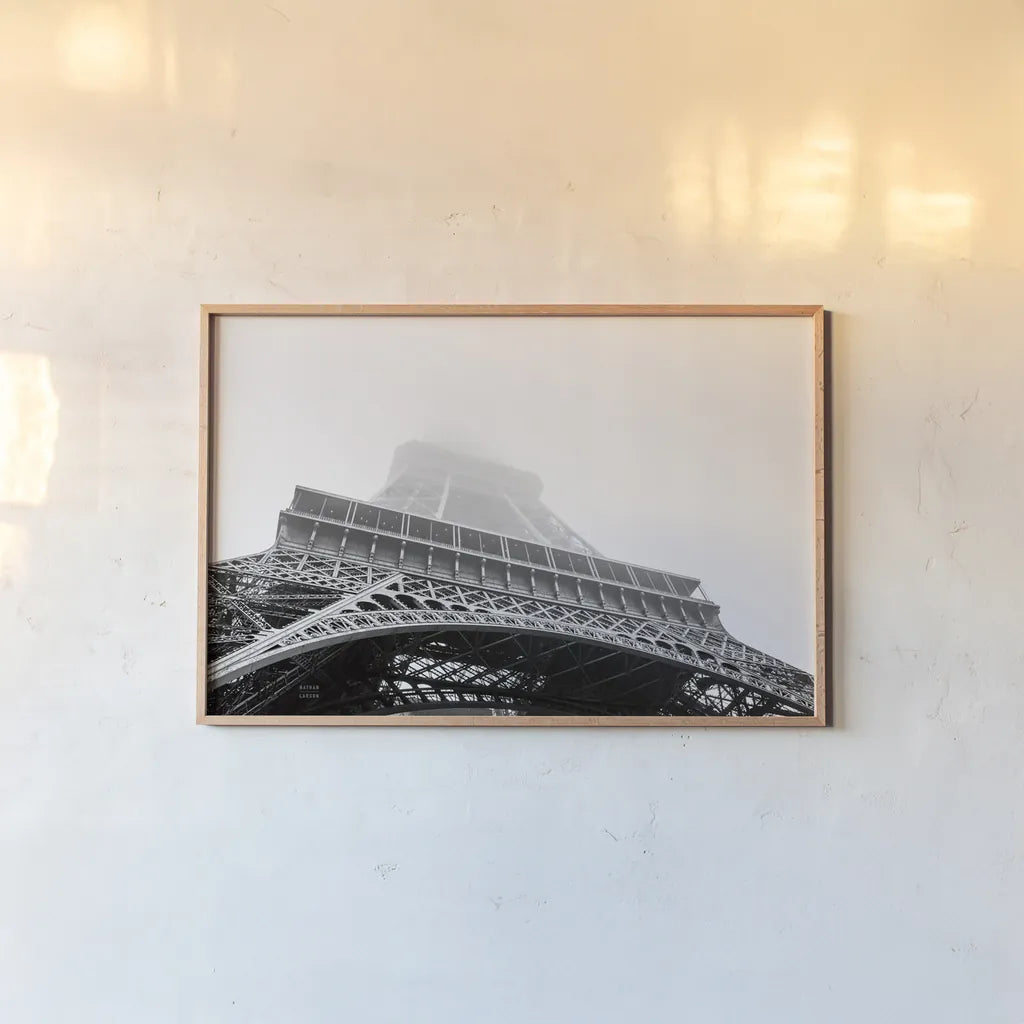 Under Eiffel Misty Day by Nathan Larson. shown as a paper print in a natural frame. Available as a archival giclee rolled canvas, fine art paper, or poster print. SKU 82299i.