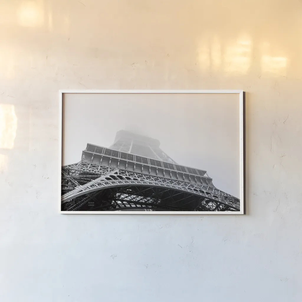 Under Eiffel Misty Day by Nathan Larson. shown as a paper print in a white frame. Available as a archival giclee rolled canvas, fine art paper, or poster print. SKU 82299i.