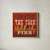 The Cook is On Fire by Pela Studio. Shown in a natural wood glass frame for a timeless modern aesthetic. Available as an archival giclee rolled canvas, fine art paper, or poster print. SKU 92148a.