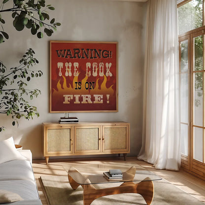 The Cook is On Fire by Pela Studio. Shown in a natural wood frame in a cozy modern living room. Available as an archival giclee rolled canvas, fine art paper, or poster print. SKU 92148a.