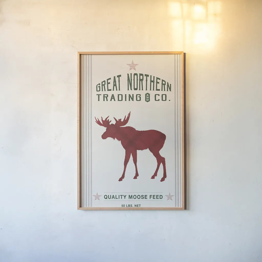 Northern Trading Moose Feed v2 by Sue Schlabach. shown as a paper print in a natural frame. Available as a archival giclee rolled canvas, fine art paper, or poster print. SKU 65049h.