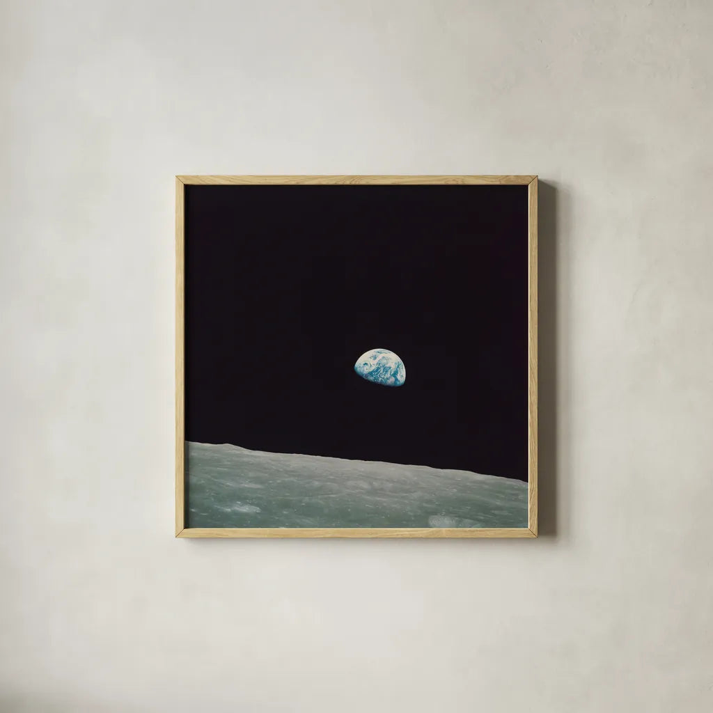 First Earth Rise by Wild Apple Portfolio. Shown in a natural wood glass frame for a timeless modern aesthetic. Available as an archival giclee rolled canvas, fine art paper, or poster print. SKU 84536a.