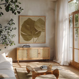 Ornate Monstera Leaf II by Wild Apple Portfolio. Shown in a natural wood frame in a cozy modern living room. Available as an archival giclee rolled canvas, fine art paper, or poster print. SKU 37202a.